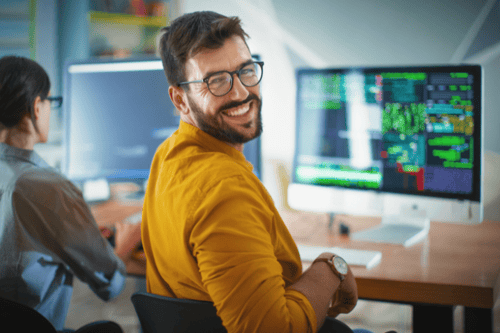 Man at a computer in a yellow shirt smiling back at the camera