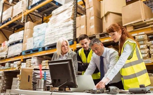 team in warehouse looking at computer discussing pricing